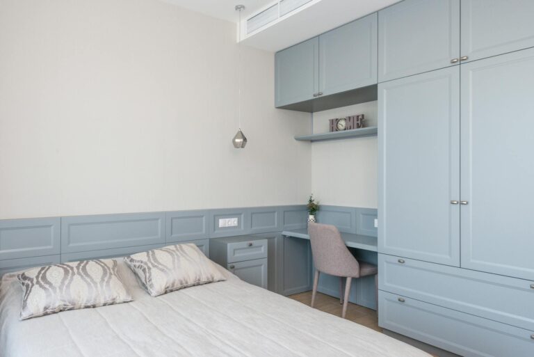 Stylish bedroom features built-in cabinetry, soft blue tones, and a cozy workspace.